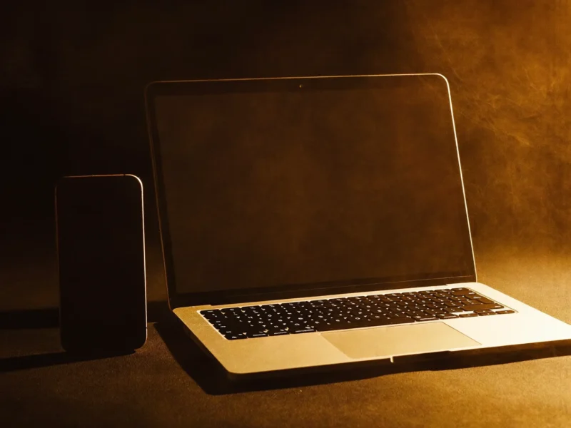 Um celular e um notebook lado a lado sobre uma mesa escura, iluminados por uma luz âmbar